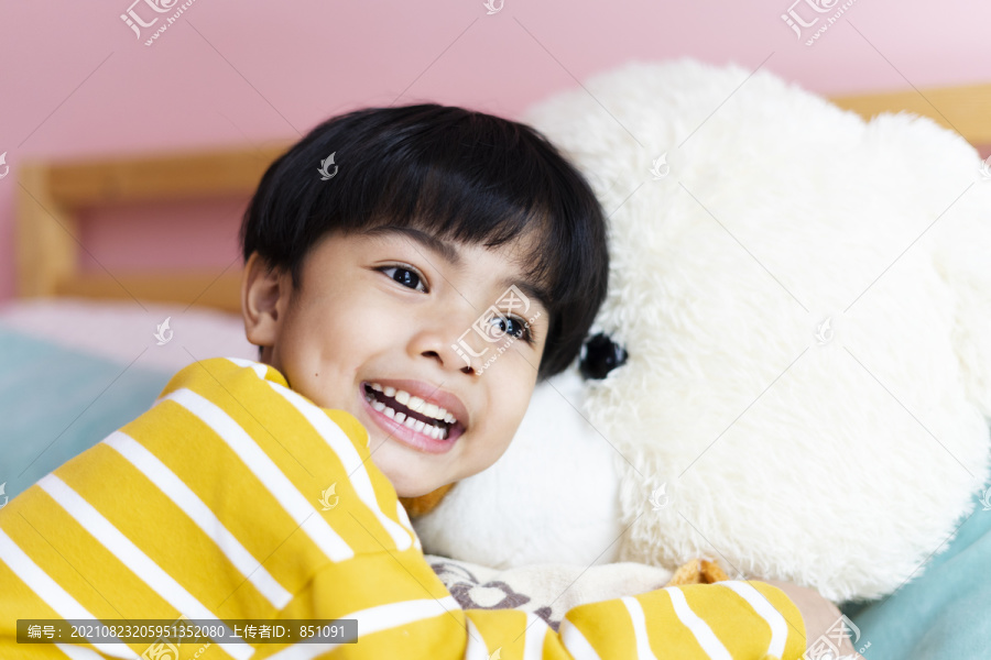 亚洲小男孩在卧室拥抱毛茸茸的大熊娃娃。