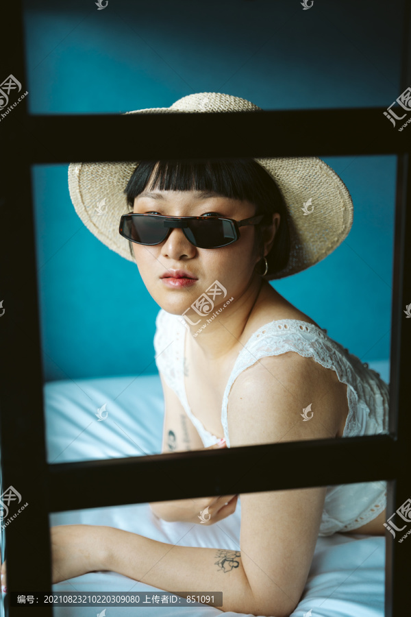 床上戴着太阳镜和帽子的快活的亚洲短发女人的肖像。