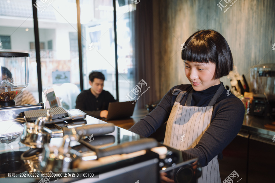 在自助餐厅为顾客煮咖啡的亚洲短发女咖啡师。