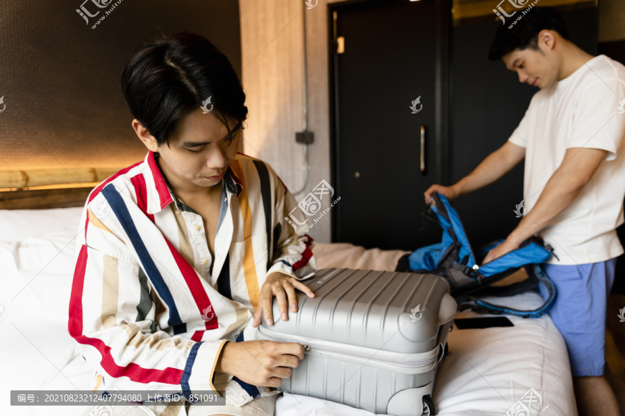 两名亚洲人在卧室的行李里收拾东西准备旅行。