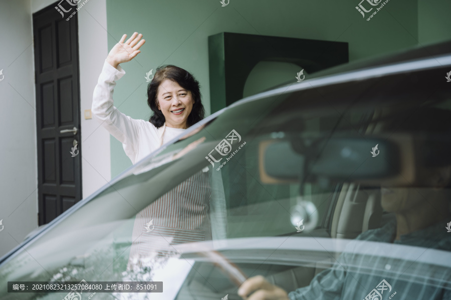 快乐的亚洲老太太在前门向丈夫挥手道别。