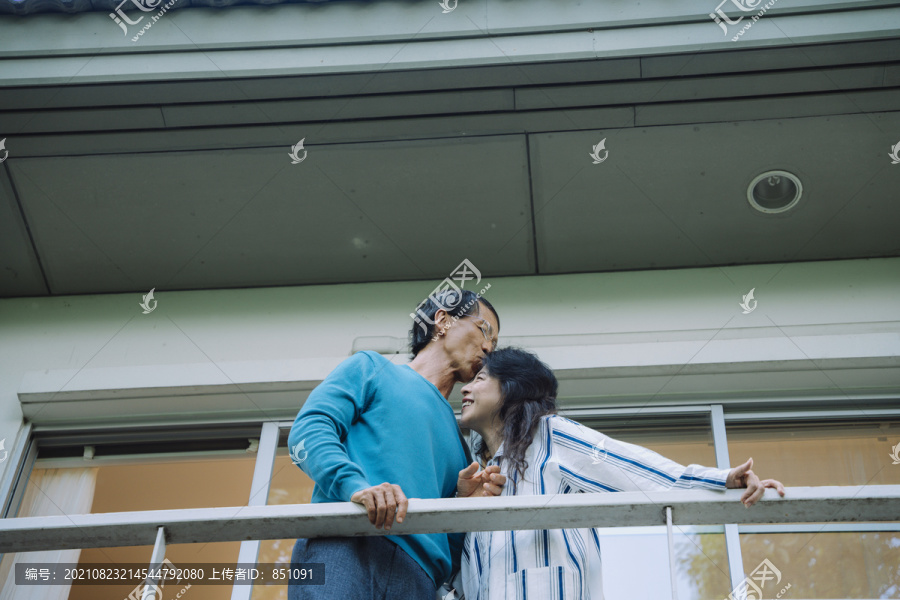 亚洲老年夫妇在家阳台上拥抱亲吻。