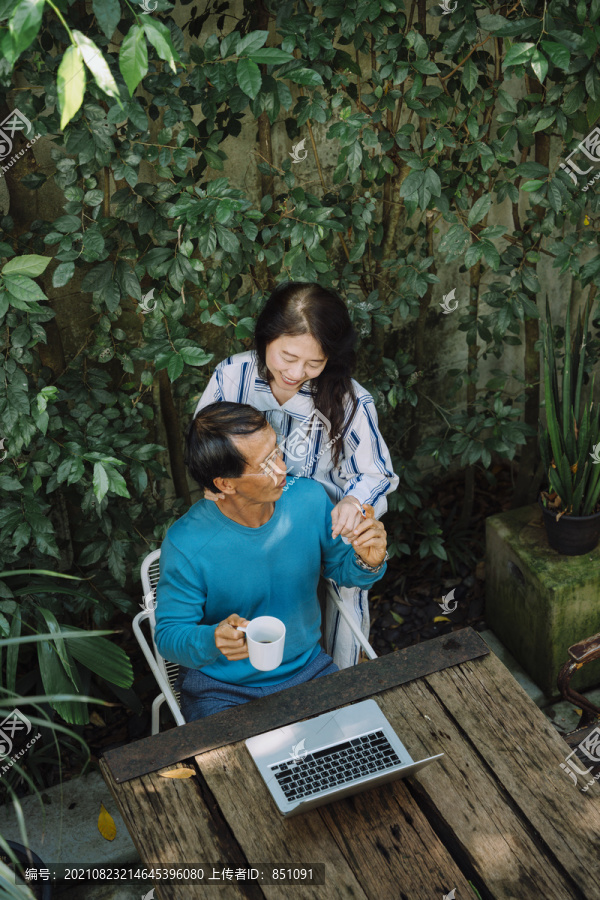 亚洲老夫妇在公园里，看着笔记本电脑，享受着浪漫的时刻。