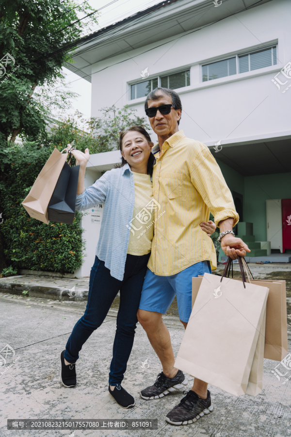 亚洲资深夫妇提着购物纸袋。