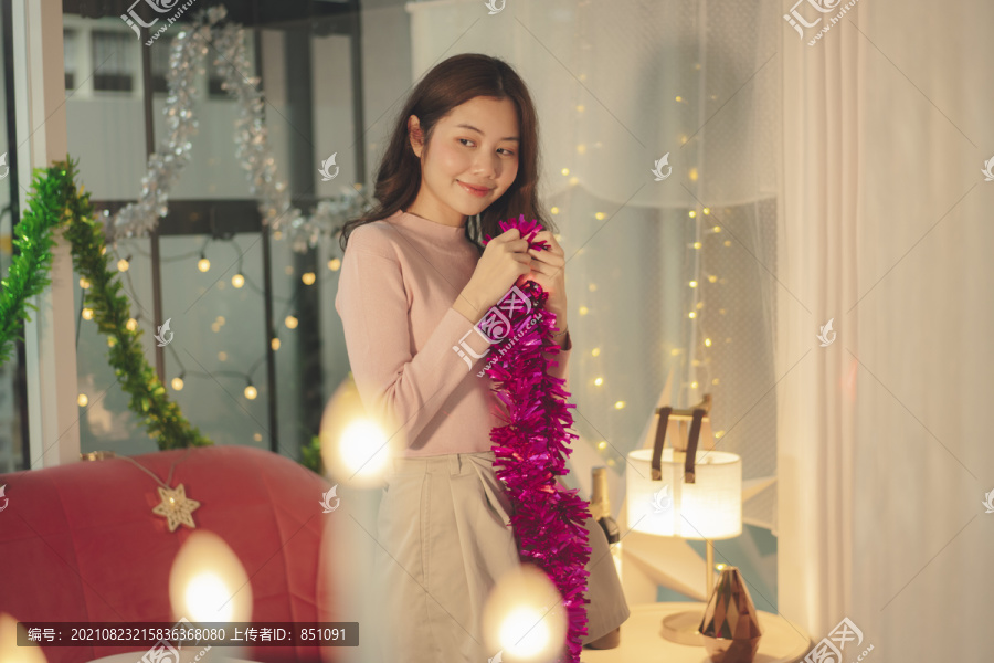 晚上，一位年轻的亚洲女士穿着粉色毛衣，用圣诞道具装饰她的房间。