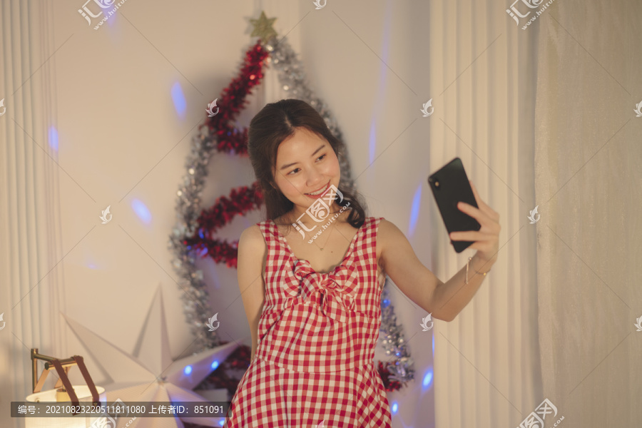 美丽的亚洲年轻女子黑发在圣诞派对上用智能手机自拍。