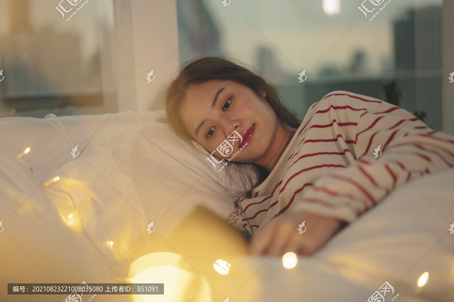 美丽的亚洲年轻女子黑头发在床上看书，带着黄色的灯光。
