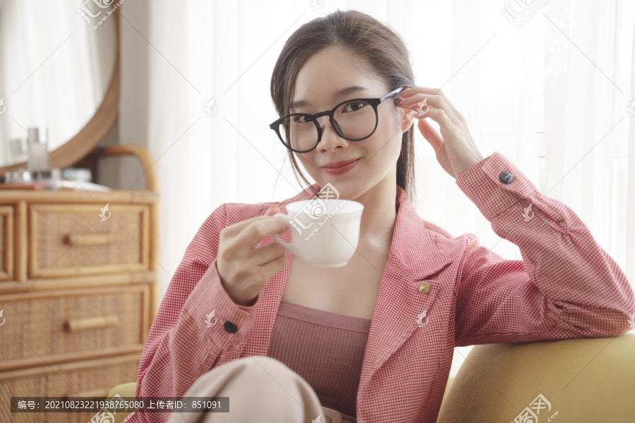 年轻的亚洲美女穿着粉色夹克，戴着眼镜，手里拿着一杯咖啡。