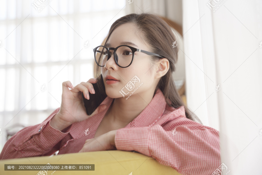 年轻的亚洲美女戴着眼镜在家里打电话。在家工作的概念。