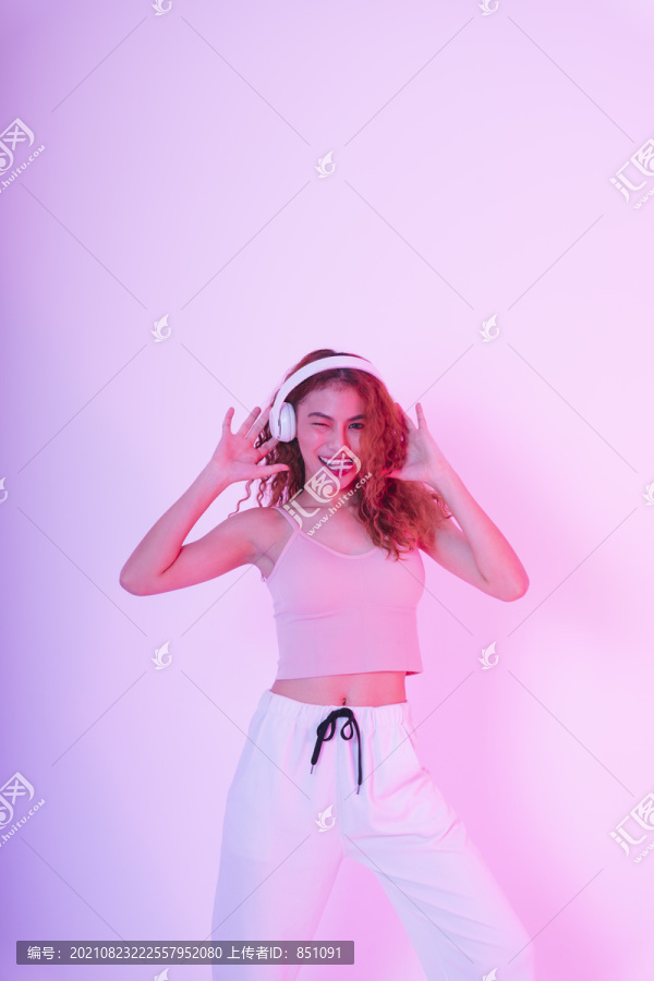 年轻的亚洲女孩穿着粉红色的衣服，在霓虹灯的背景下听音乐跳舞。