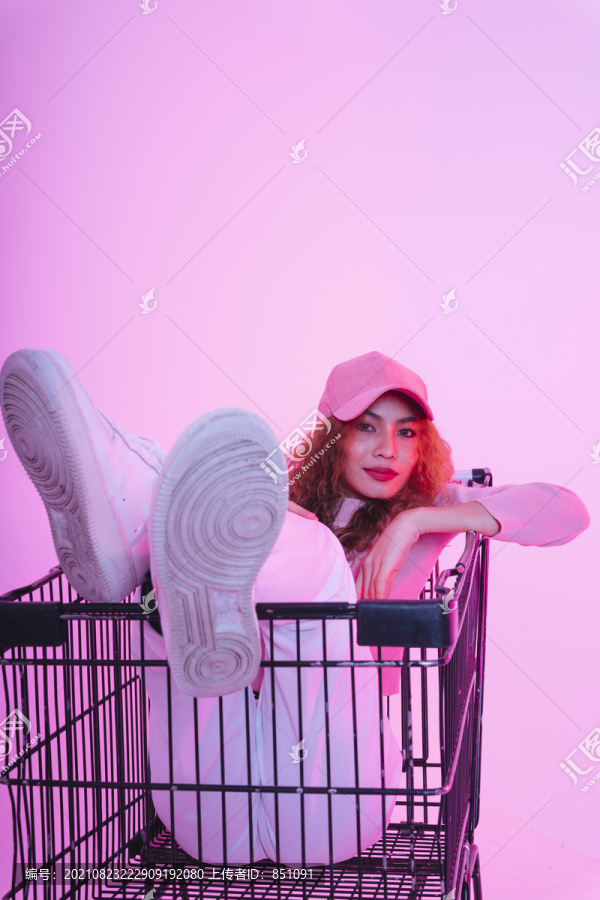 亚洲年轻卷发女子戴帽子坐在购物车上的肖像。