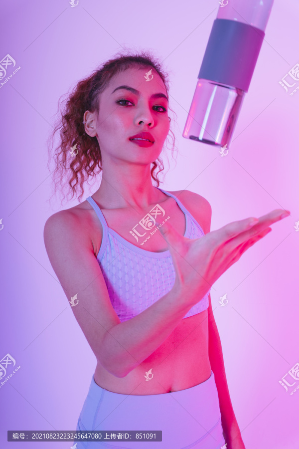 年轻的亚洲健康卷发女性肖像，粉红色背景，带水瓶。