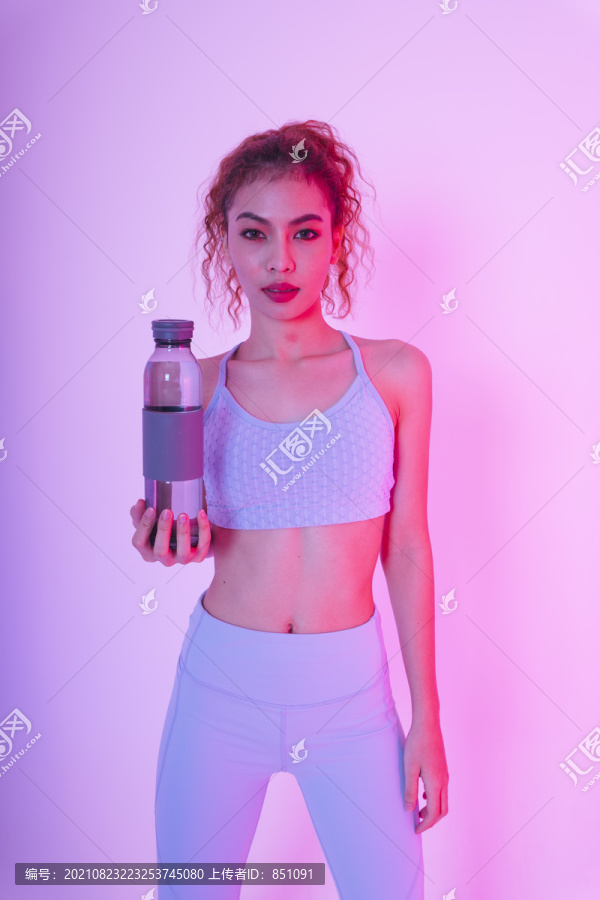 年轻的亚洲健康卷发女性肖像，粉红色背景，带水瓶。
