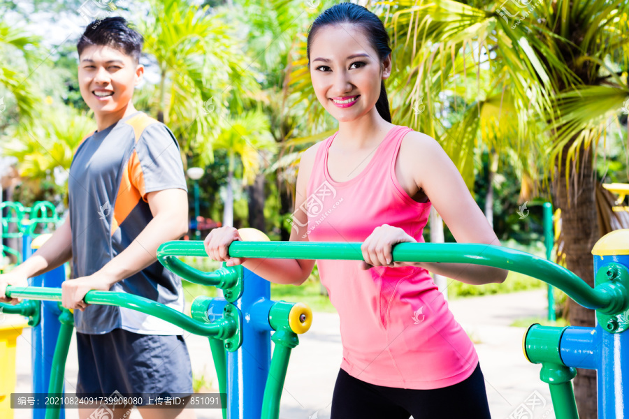 中国亚裔男子和女子在室外体育馆公共交叉训练器上的健身训练