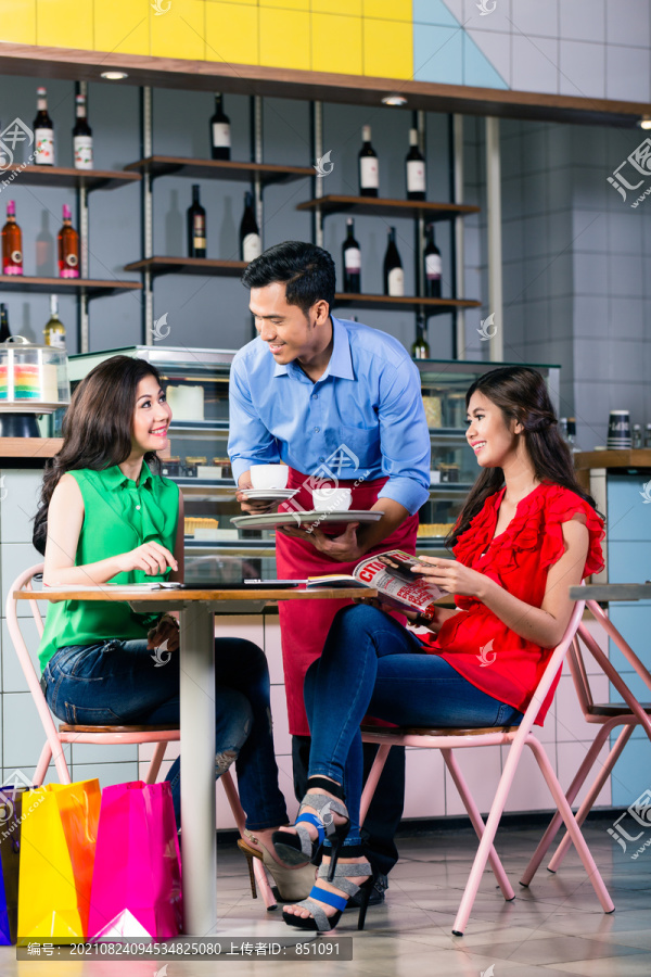 在一家时髦的咖啡馆里，一位英俊、礼貌的服务员在两位漂亮的年轻女士的餐桌上端咖啡时微笑着