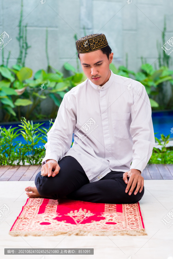 亚洲穆斯林男子穿着传统服装在地毯上祈祷