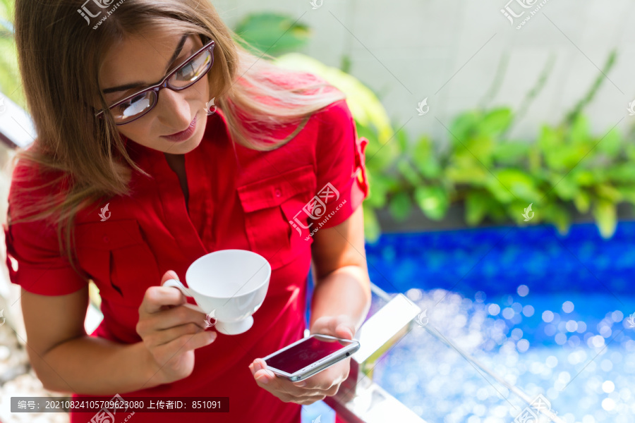 热带地区，一位女士一边在阳台上喝咖啡，一边用智能手机阅读邮件