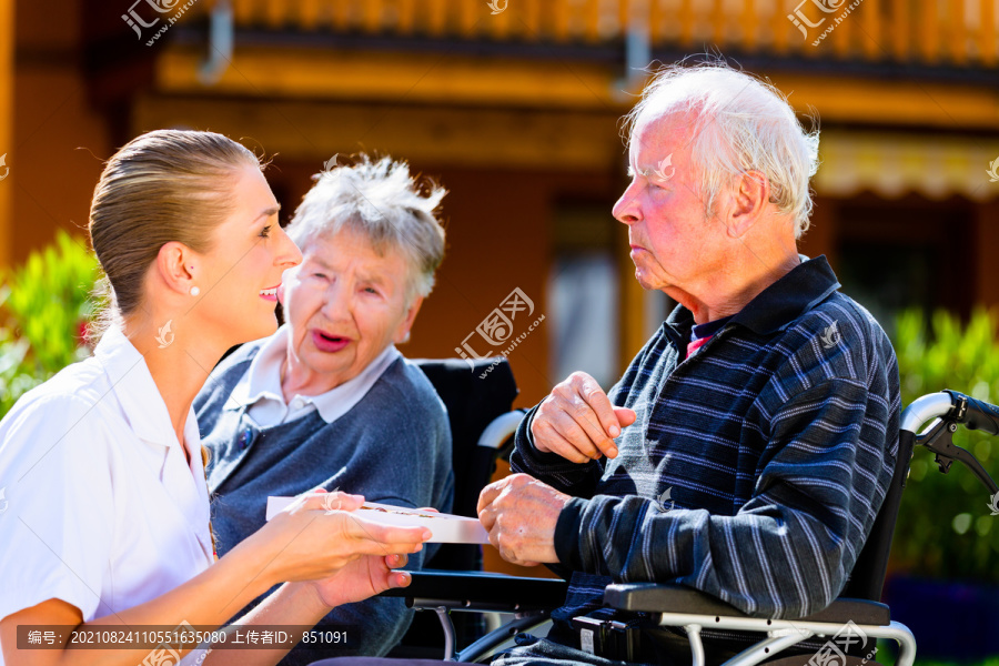 老人们，一对男女坐在轮椅上，在疗养院的花园里吃糖果