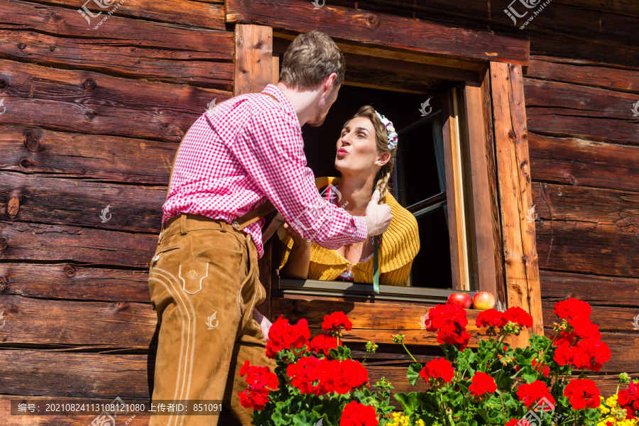一对穿着传统服装的情侣在山间小屋的窗户前相爱