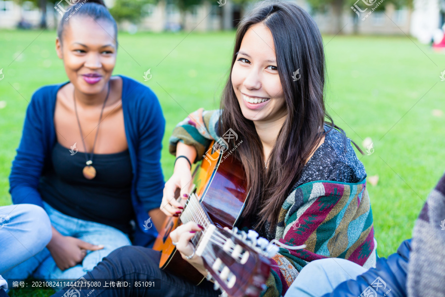 朋友们在公园里唱歌，和一个弹吉他的女孩一起玩，这是一个由非洲、亚洲和高加索人组成的多元化团体