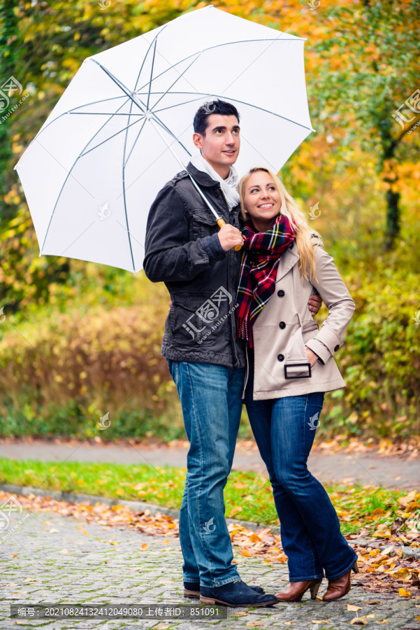 这对夫妇正享受着秋天，他们带着雨伞在雨中散步