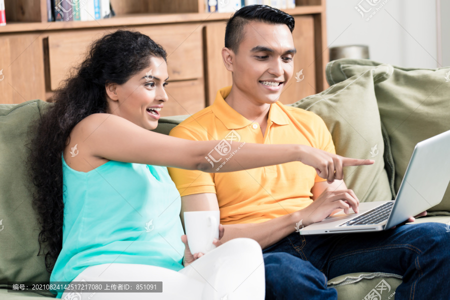 一位微笑的女士指着笔记本电脑屏幕向她的丈夫展示一些东西