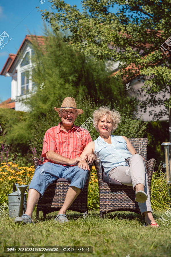 一对相爱的快乐老年夫妇坐在椅子上，在夏日阳光明媚的日子里，一起在家里的花园里放松的低角度照片