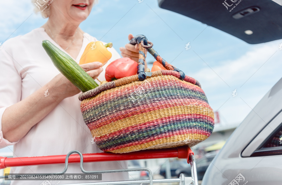一个快乐的老妇人在超市购物后拿着一个装满新鲜营养蔬菜的草篮的低视角照片