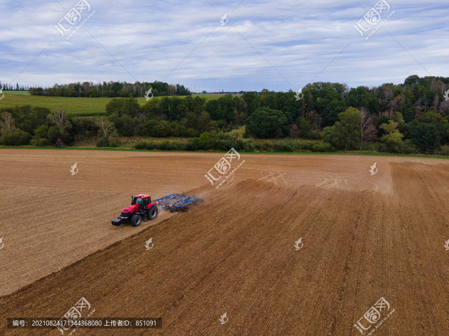 农民用拖拉机在广阔的土地上耕作，空中射击