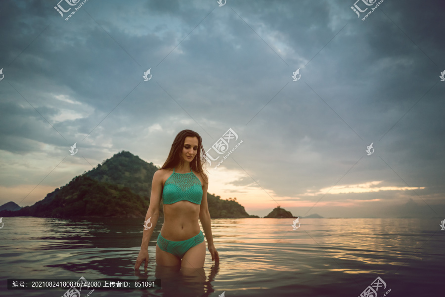 在海滩度假时，日落时在热带海洋中沐浴的女人