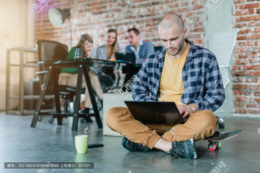 在一家初创公司里，一位时髦的员工坐在滑板上，笔记本电脑和同事们一起编码