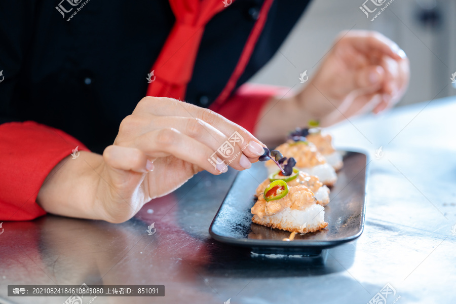 女厨师在一个黑色陶瓷盘子里给完成的开胃菜调味