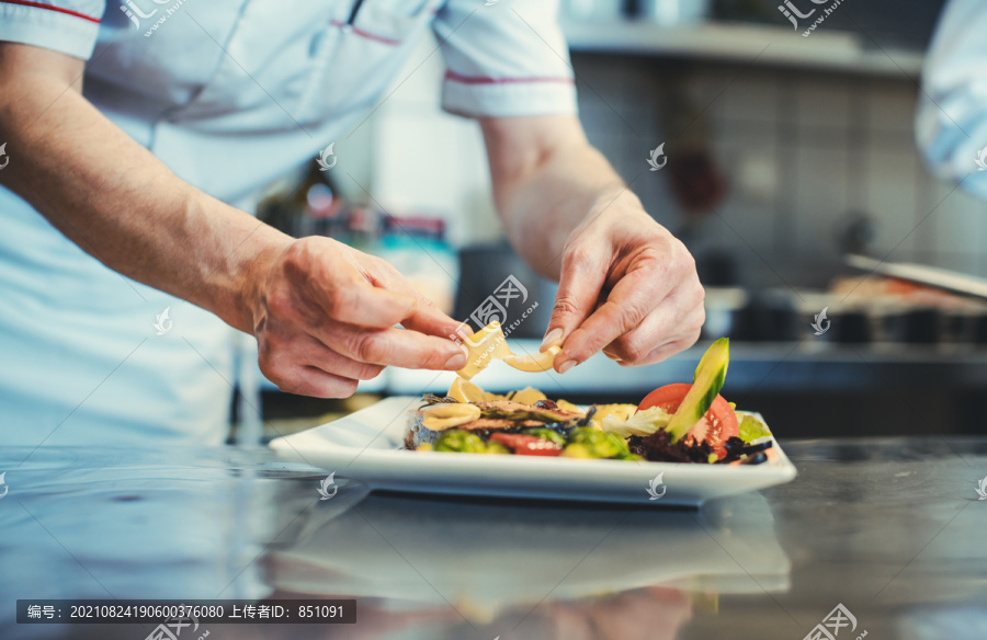 骄傲的厨师在餐厅用药草装饰一道几乎完成的菜