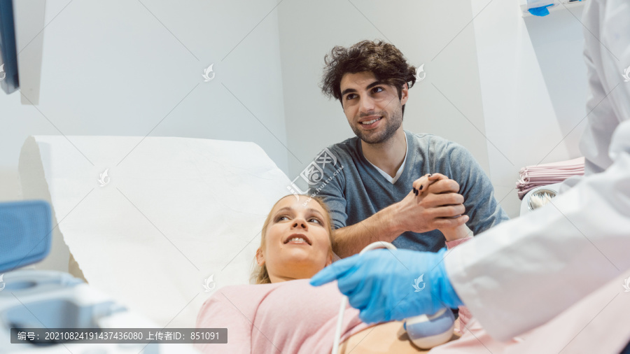 当妻子怀孕时，一对夫妇手牵手在生育诊所，两人都在看超声波屏幕