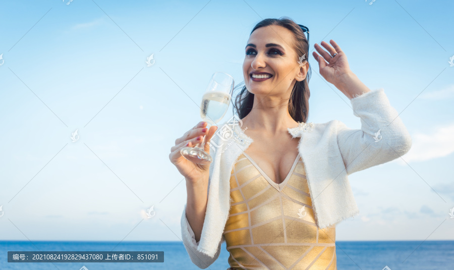 在海滩上的一个聚会上，坐在海边的女人，手里拿着一杯香槟