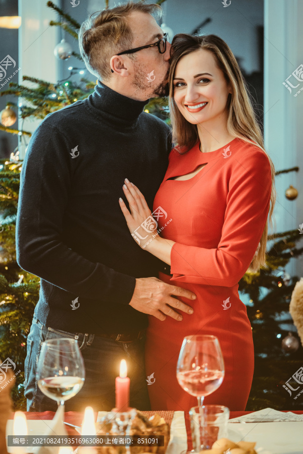 一对中年夫妇在圣诞树前摆出浪漫的姿势，带着季节性的精神
