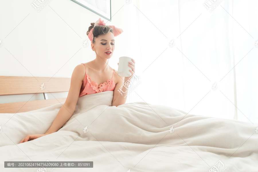 美丽的女人在床上啜饮着早晨的咖啡，开始了新的一天
