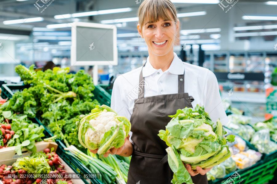超市女店员自豪地看着摄像机，展示着新鲜农产品