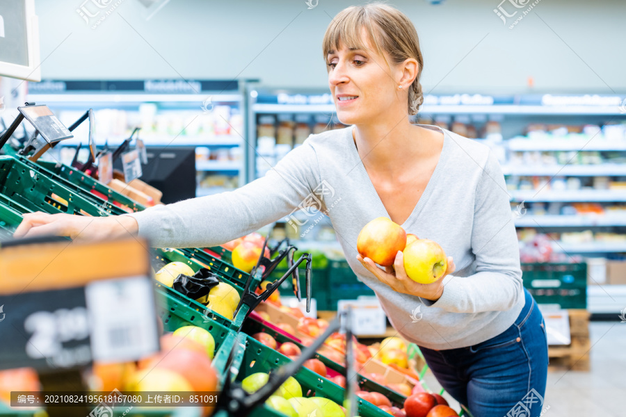 一名妇女手拿苹果在超市货架上测试新鲜水果