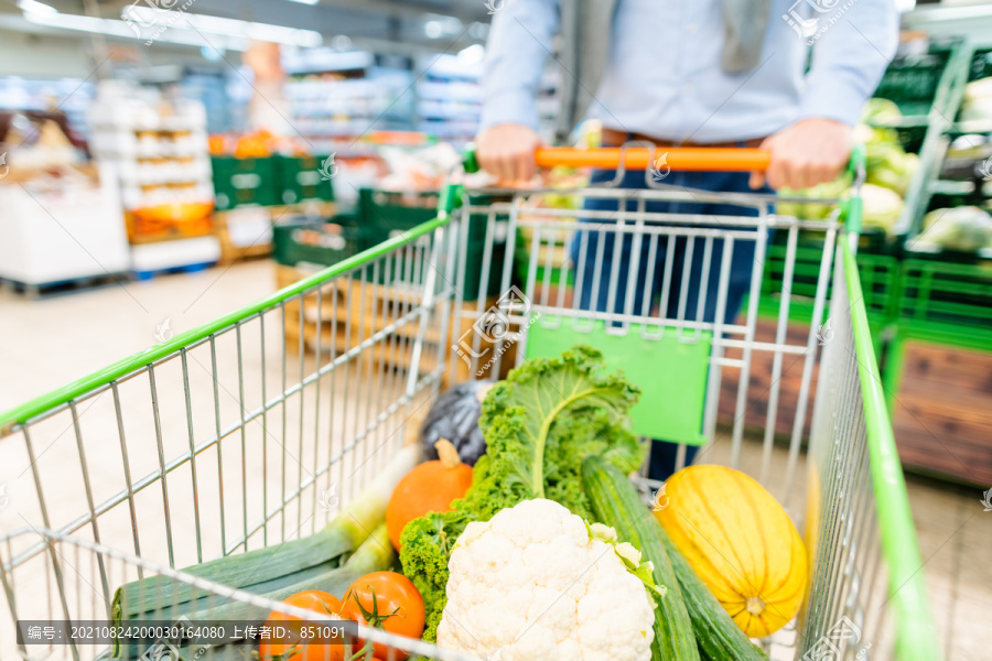 一名男子在超市购物，推着手推车，里面装满了蔬菜和杂货