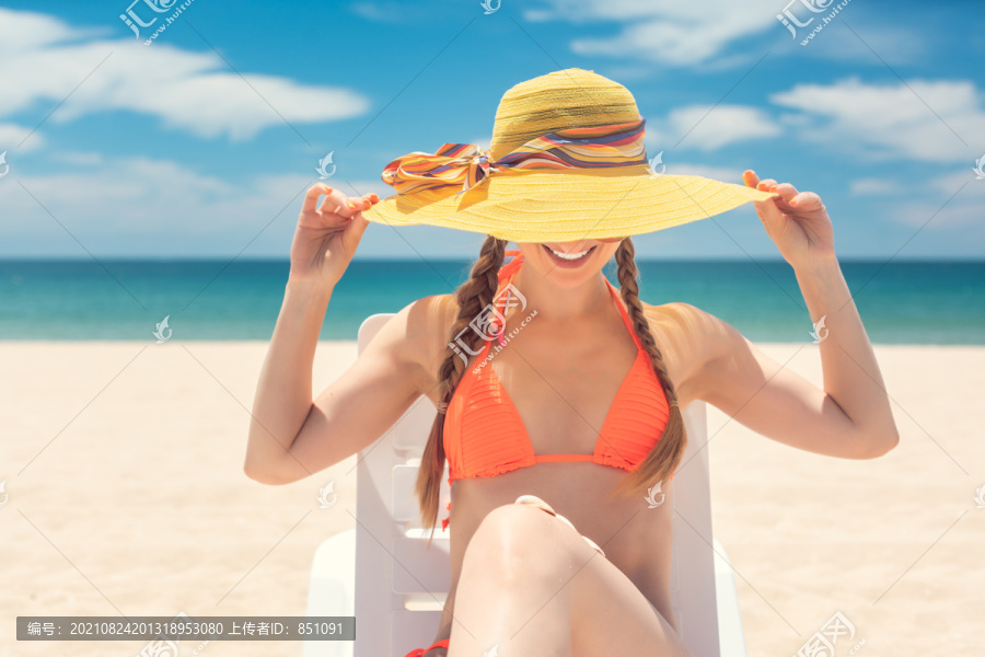 一名妇女举着帽子在海边的海滩上晒太阳