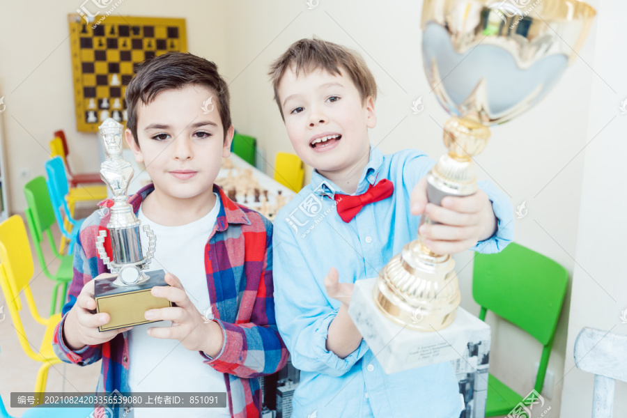两个男孩拿着奖杯在空中赢得了国际象棋比赛
