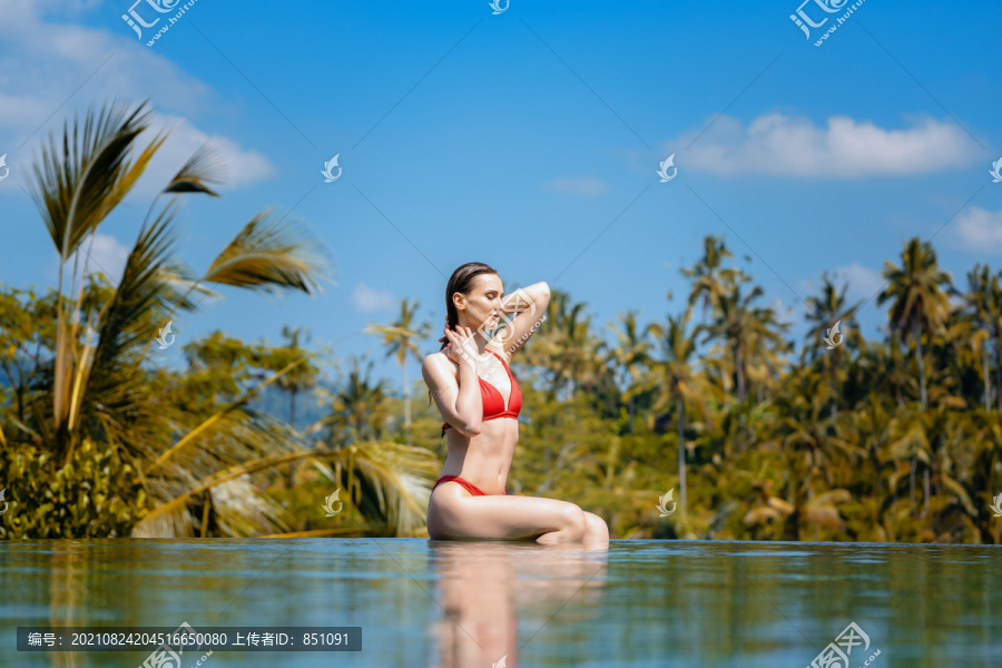 热带度假的女人坐在棕榈树前的水池里