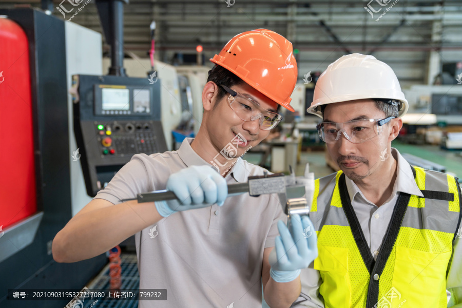 两个工程师穿保护工作服戴着安全帽在工厂工作