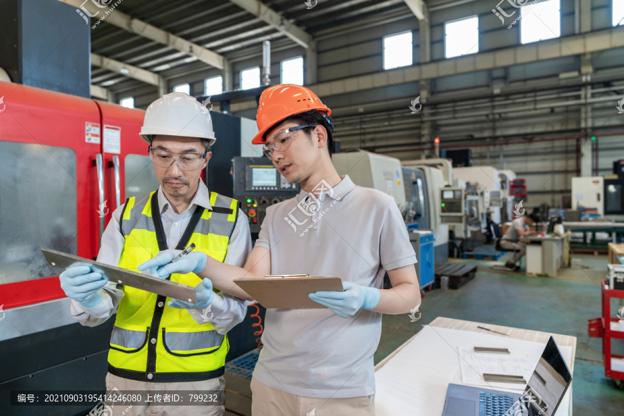 两个工程师穿保护工作服戴着安全帽在工厂做测量