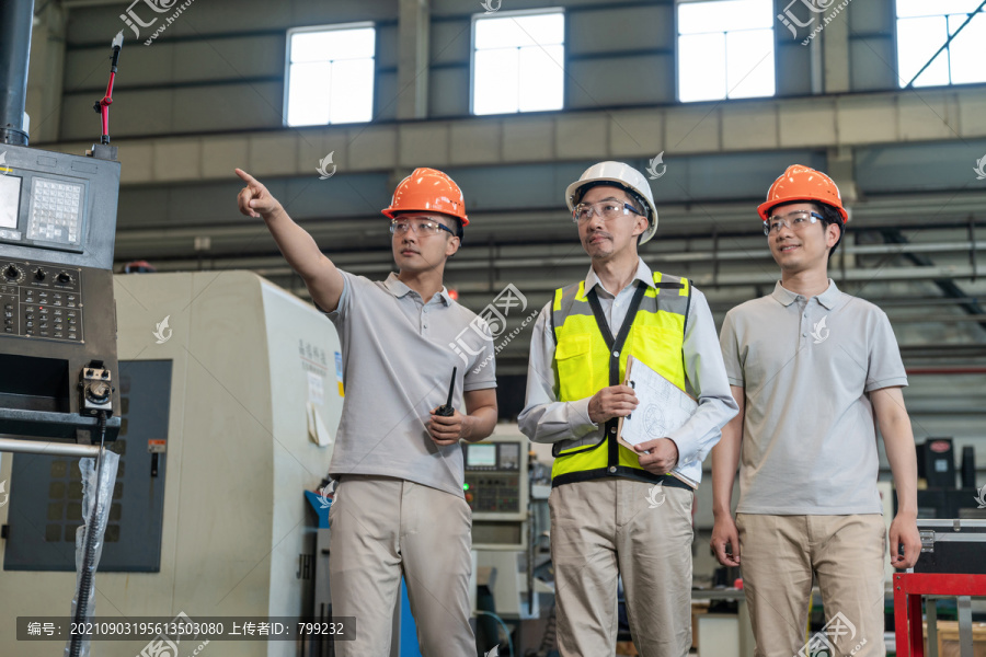 三个工程师穿保护工作服戴着安全帽在工厂工作