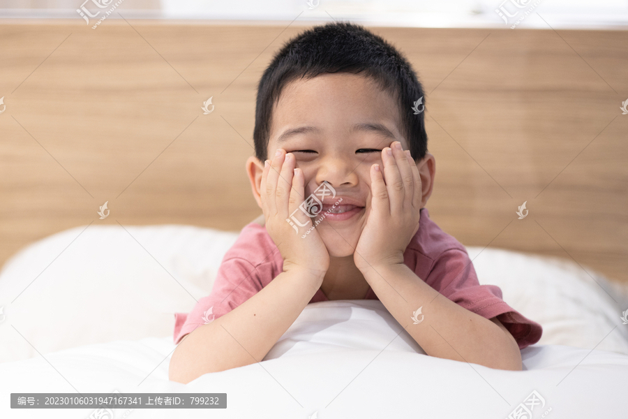 一个小男孩趴在床上托着腮帮子微笑